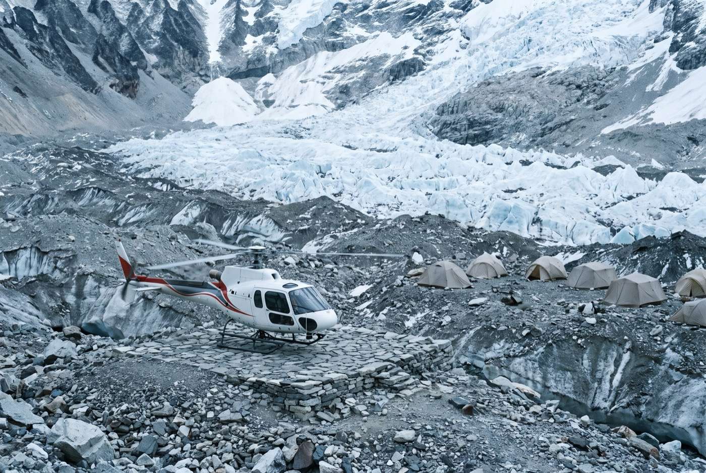 A single-engine helicopter standing on a stone pad on glacial moraine, a few plain dome tents to one side, a crevassed icefall rising behind.