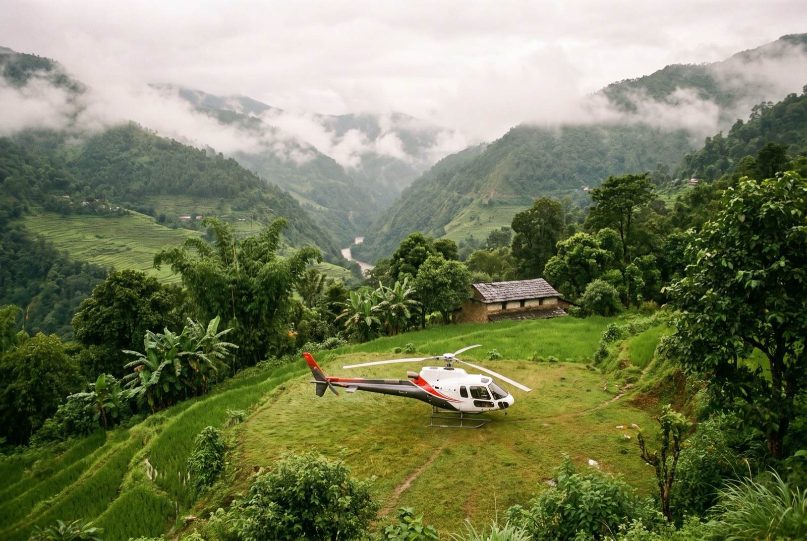 A small white single-engine helicopter standing on a grass pad cut into a terraced hillside, green monsoon ridges and cloud behind it.