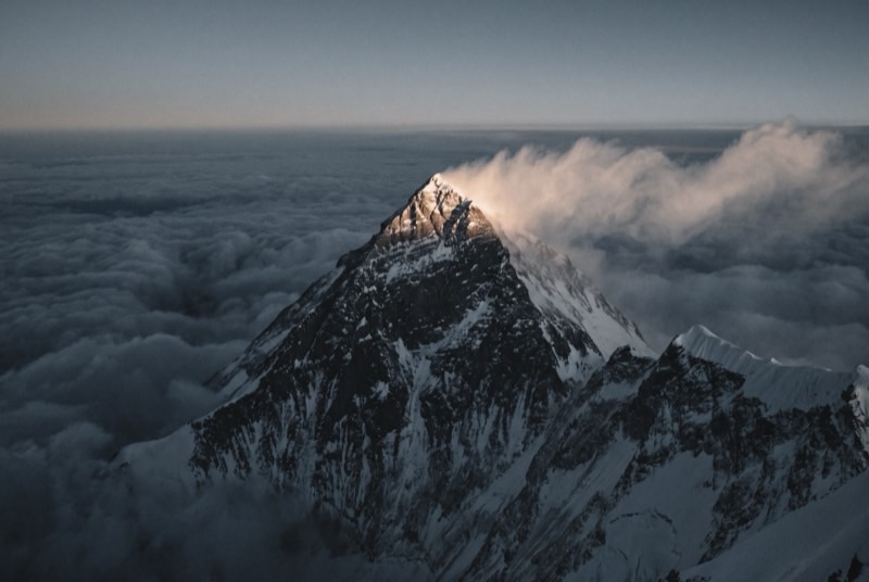 The summit pyramid of Everest above a sea of cloud at first light, its snow plume streaming east