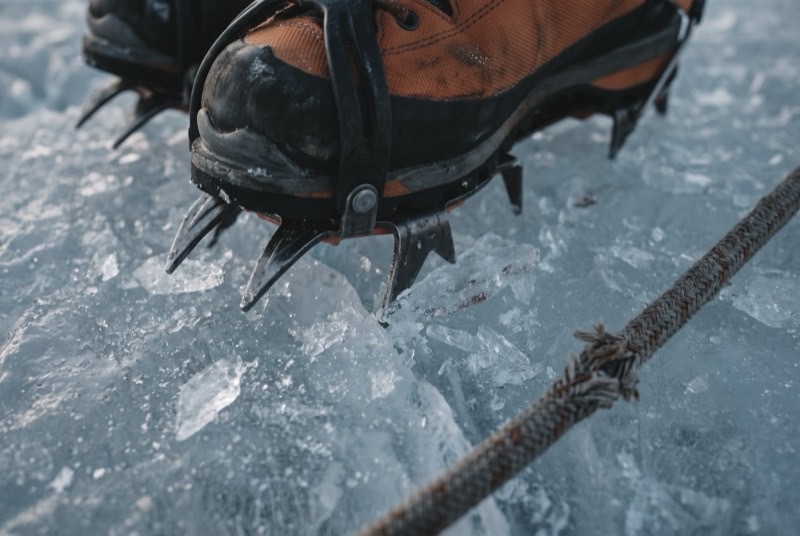 Crampon front points bitten into blue glacial ice beside the frayed sheath of a fixed rope.