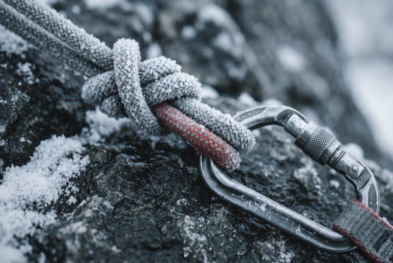 A figure-of-eight knot furred with frost, tied into a frozen rope and clipped to a steel locking carabiner