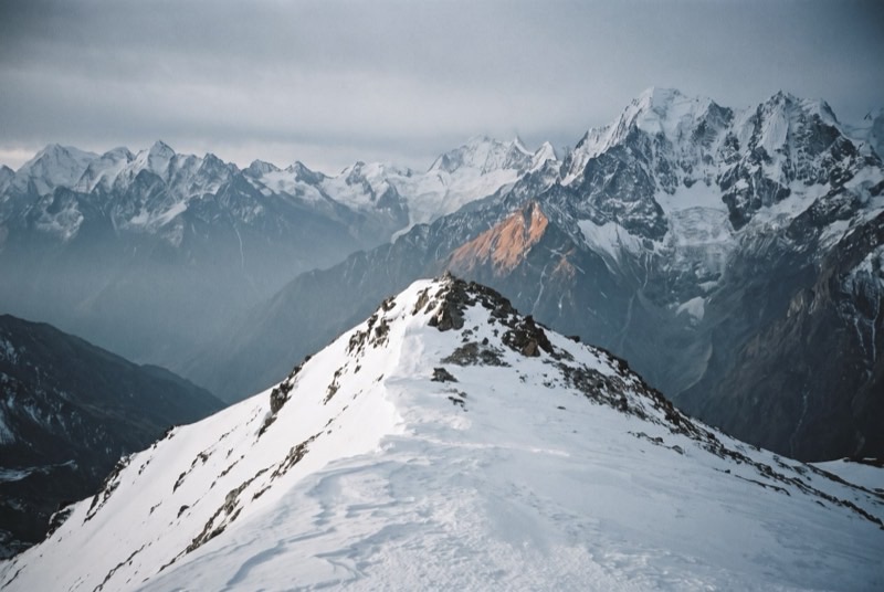 Yala Peak's wind-scoured summit ridge above the Langtang valley, with ranks of higher Himalayan peaks receding into blue haze.